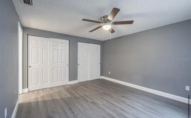 unfurnished bedroom featuring two closets, wood-type flooring, a textured ceiling, and ceiling fan