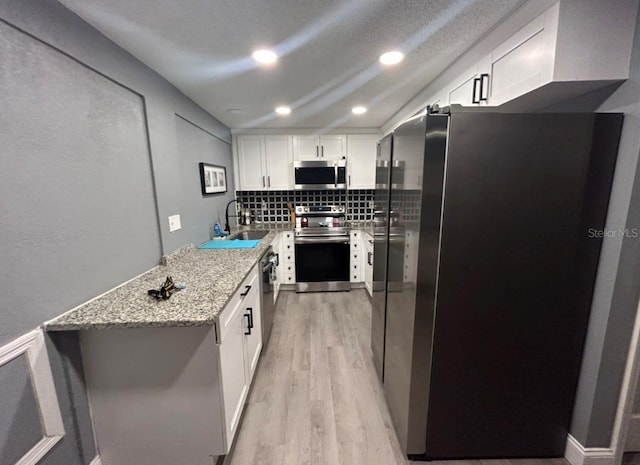 kitchen with light stone counters, stainless steel appliances, white cabinetry, light wood-style floors, and tasteful backsplash