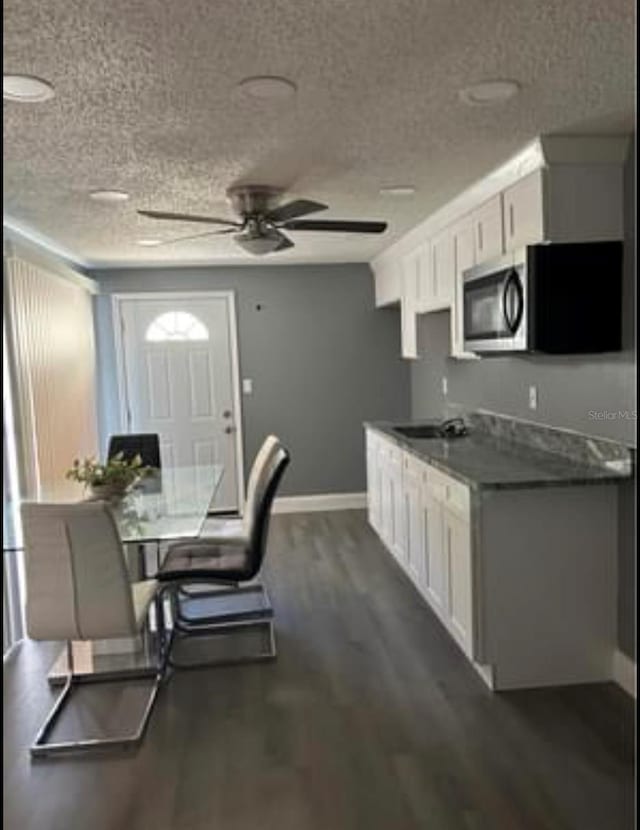 kitchen featuring a sink, stainless steel microwave, dark wood finished floors, and white cabinetry