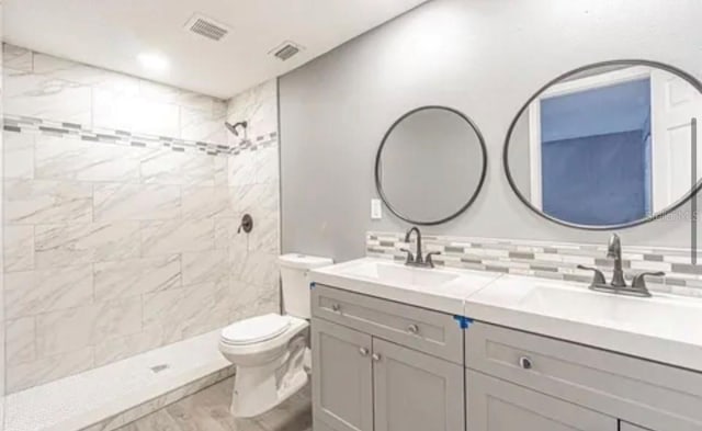 bathroom with tiled shower, toilet, decorative backsplash, and double sink vanity