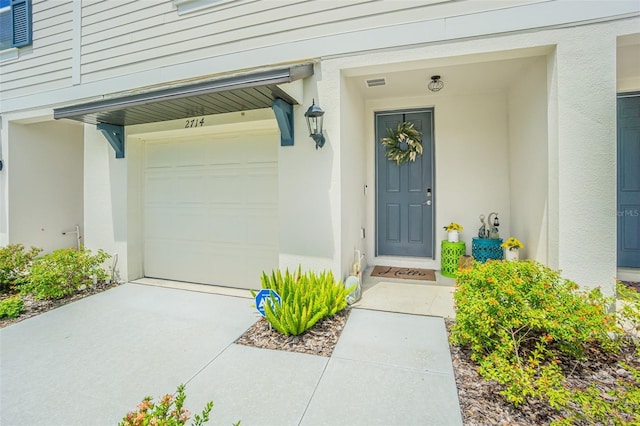 property entrance with visible vents, driveway, and stucco siding