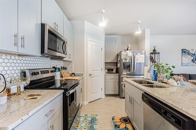 kitchen featuring appliances with stainless steel finishes, sink, gray cabinets, backsplash, and light stone countertops