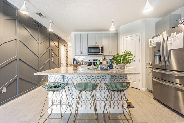 kitchen featuring tasteful backsplash, a kitchen bar, light stone countertops, appliances with stainless steel finishes, and gray cabinetry