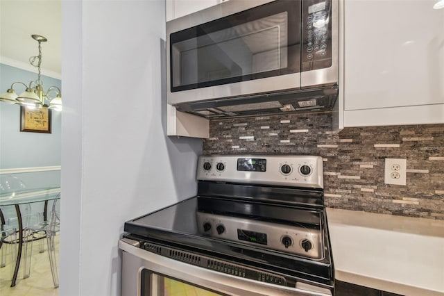 kitchen with crown molding, hanging light fixtures, stainless steel appliances, decorative backsplash, and white cabinets