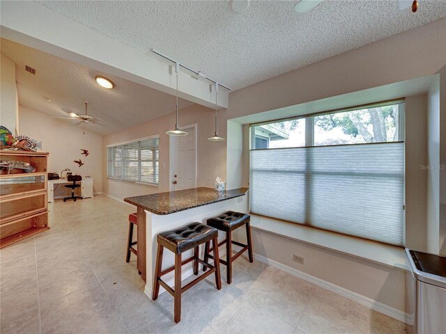 kitchen with kitchen peninsula, a breakfast bar, a textured ceiling, ceiling fan, and pendant lighting