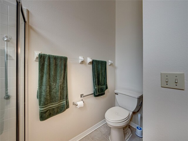 bathroom with tile patterned flooring, toilet, and a shower with door