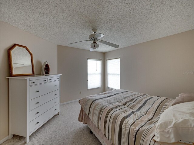 bedroom featuring ceiling fan, light colored carpet, and a textured ceiling