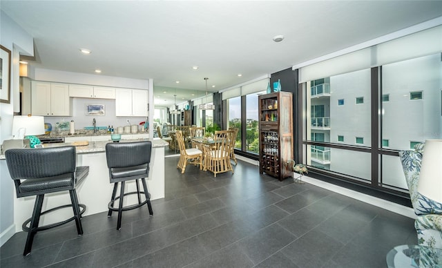 kitchen with white cabinetry, decorative light fixtures, a breakfast bar area, light stone countertops, and a wall of windows