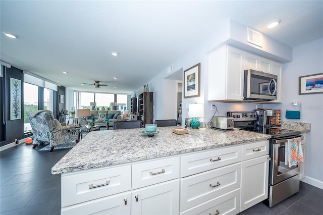 kitchen with appliances with stainless steel finishes, light stone countertops, ceiling fan, and white cabinetry