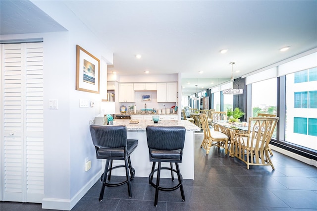 kitchen with white cabinetry, pendant lighting, light stone counters, a breakfast bar, and dark tile patterned flooring