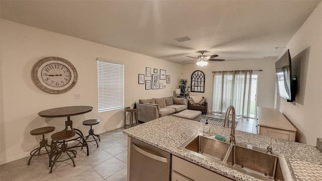 kitchen with sink, light tile patterned floors, stainless steel dishwasher, light stone countertops, and ceiling fan