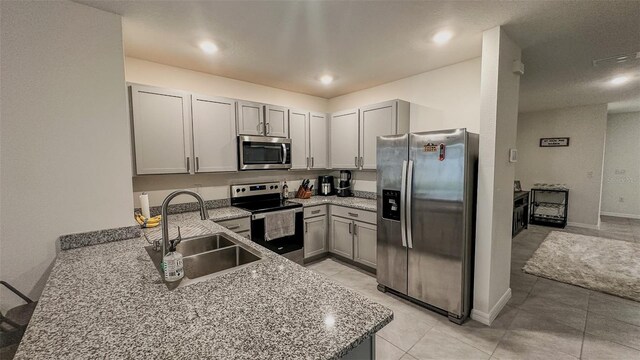 kitchen with appliances with stainless steel finishes, gray cabinetry, sink, light tile patterned floors, and light stone countertops