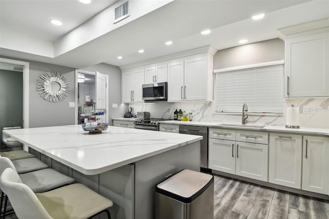 kitchen featuring a kitchen bar, a kitchen island, stainless steel appliances, light stone countertops, and white cabinets