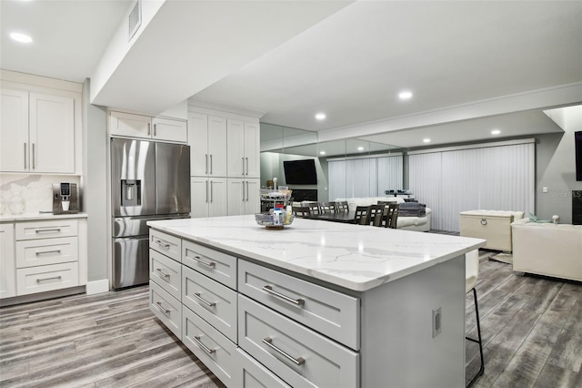 kitchen with a kitchen breakfast bar, stainless steel refrigerator with ice dispenser, light stone countertops, white cabinets, and a kitchen island