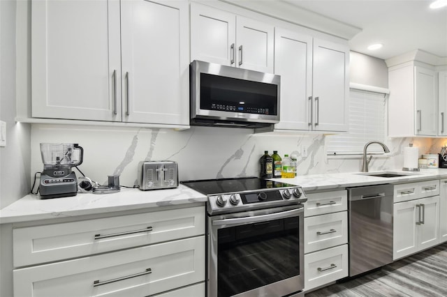 kitchen featuring sink, white cabinetry, stainless steel appliances, light stone countertops, and decorative backsplash