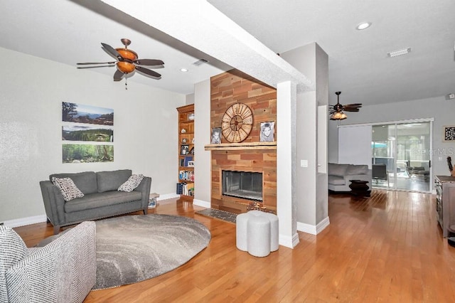 living room with a tiled fireplace, ceiling fan, and hardwood / wood-style flooring