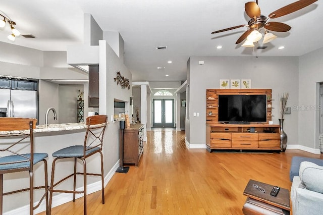 kitchen with light hardwood / wood-style flooring, stainless steel refrigerator, a kitchen bar, and ceiling fan