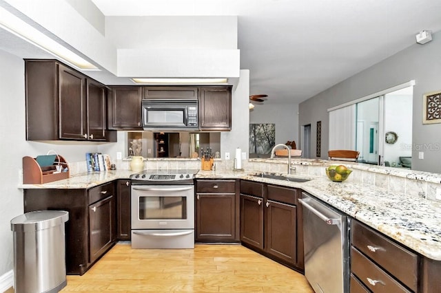 kitchen with sink, light stone countertops, light hardwood / wood-style floors, appliances with stainless steel finishes, and kitchen peninsula