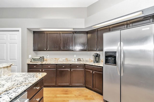 kitchen with dark brown cabinets, light stone counters, appliances with stainless steel finishes, and light wood-type flooring