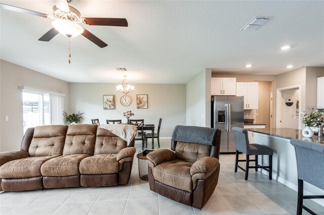 tiled living room with a textured ceiling and ceiling fan with notable chandelier