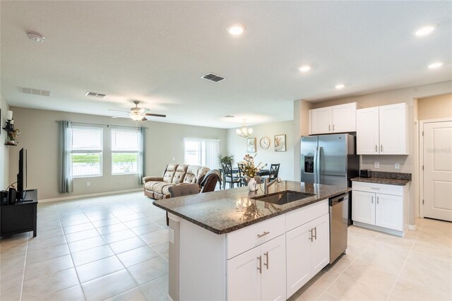 kitchen with stainless steel appliances, ceiling fan with notable chandelier, a center island with sink, light tile patterned flooring, and dark stone counters