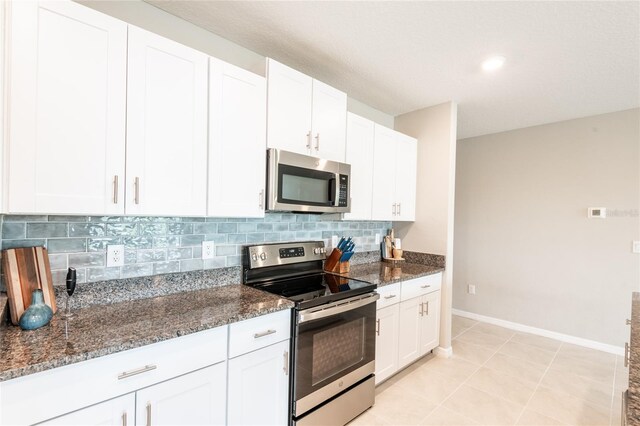 kitchen with appliances with stainless steel finishes, dark stone countertops, white cabinets, light tile patterned floors, and decorative backsplash