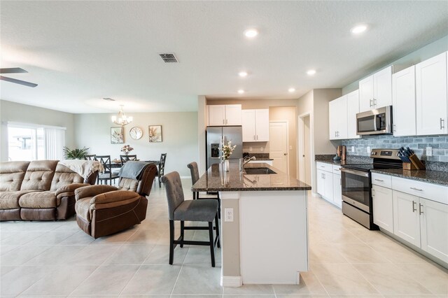 kitchen featuring ceiling fan with notable chandelier, appliances with stainless steel finishes, dark stone counters, white cabinets, and a kitchen bar