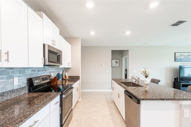 kitchen with stainless steel appliances, light tile patterned floors, white cabinets, a center island with sink, and sink