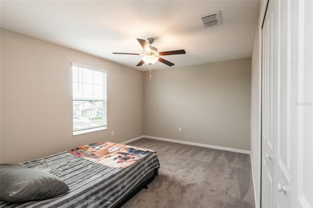 carpeted bedroom with ceiling fan and a textured ceiling