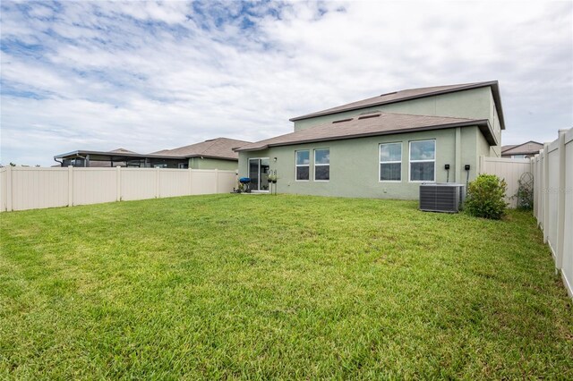 rear view of property with central AC unit and a lawn