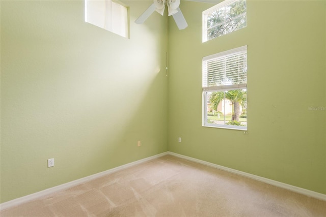 carpeted empty room featuring ceiling fan and a high ceiling