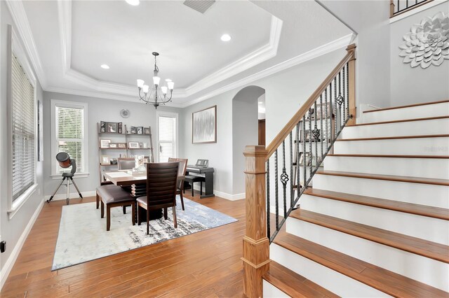 dining area featuring a chandelier, ornamental molding, light wood-type flooring, and a tray ceiling