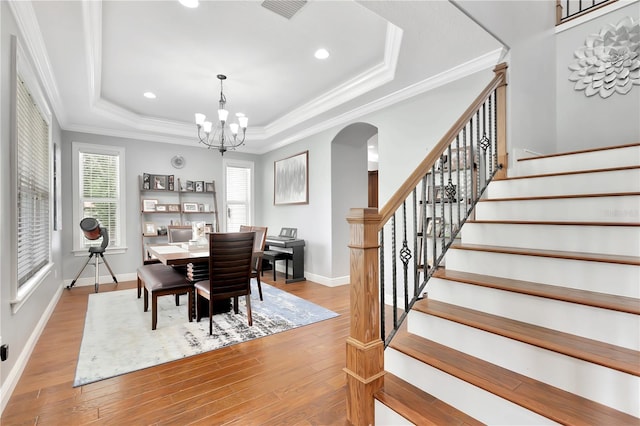 dining room with an inviting chandelier, ornamental molding, a tray ceiling, and light hardwood / wood-style flooring