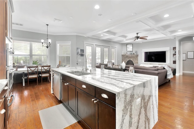 kitchen featuring a stone fireplace, sink, a kitchen island with sink, light wood-type flooring, and coffered ceiling