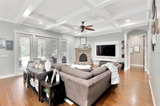 living room featuring a stone fireplace, wood-type flooring, and coffered ceiling