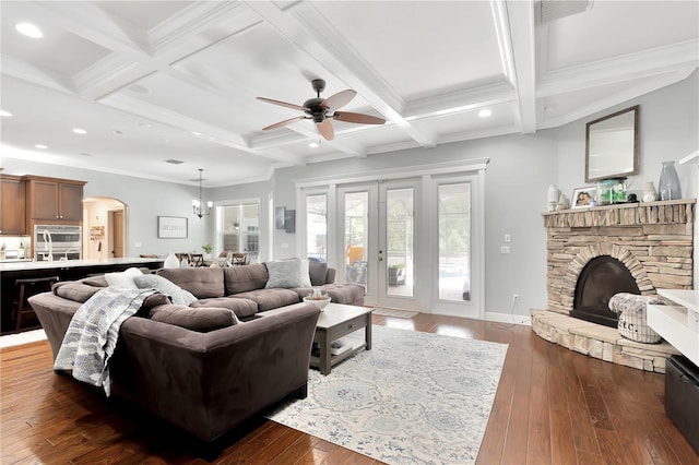 living room with a stone fireplace, dark wood-type flooring, ceiling fan, ornamental molding, and coffered ceiling