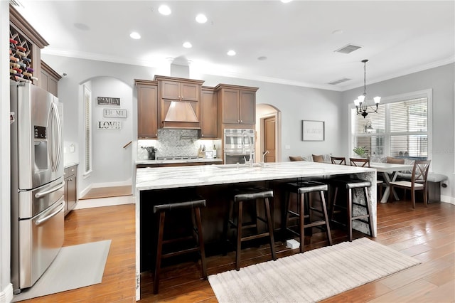 kitchen with a large island, a breakfast bar, appliances with stainless steel finishes, decorative light fixtures, and custom exhaust hood