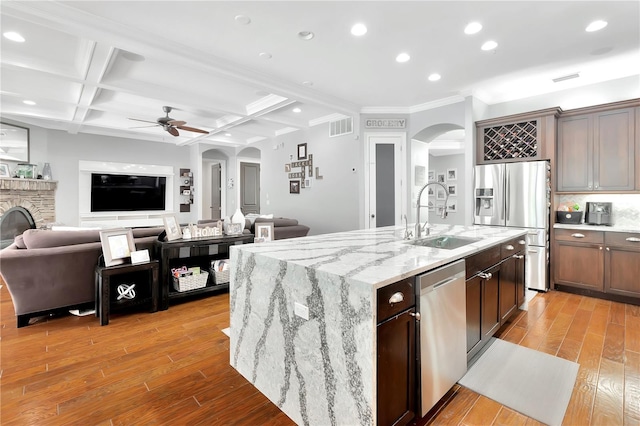 kitchen featuring appliances with stainless steel finishes, a stone fireplace, sink, light wood-type flooring, and coffered ceiling