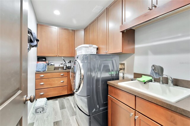 clothes washing area featuring washer / dryer, sink, light wood-type flooring, and cabinets