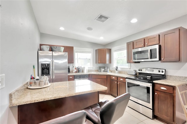 kitchen with a breakfast bar, sink, light stone counters, light tile patterned floors, and stainless steel appliances