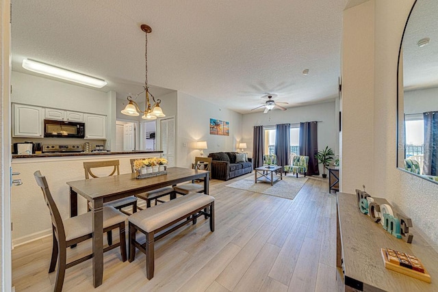 dining area with a textured ceiling, ceiling fan with notable chandelier, and light hardwood / wood-style flooring