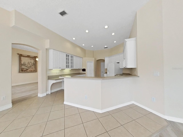 kitchen with white cabinets, white refrigerator with ice dispenser, light tile patterned floors, and kitchen peninsula