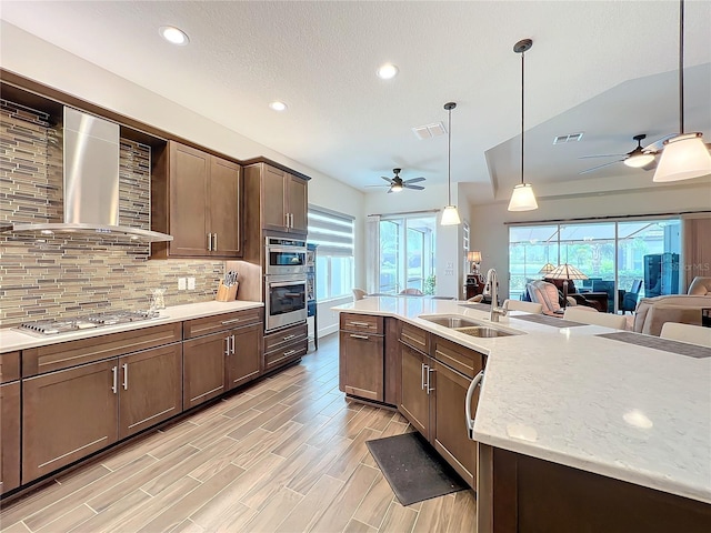 kitchen with pendant lighting, sink, wall chimney range hood, stainless steel appliances, and light stone countertops