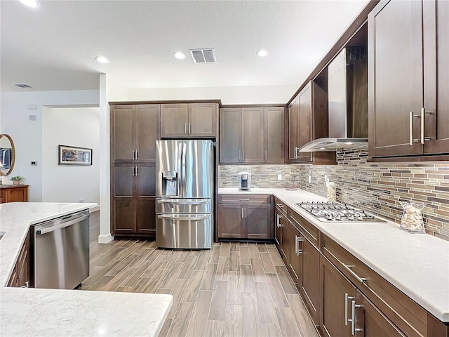 kitchen with wall chimney exhaust hood, tasteful backsplash, dark brown cabinets, a textured ceiling, and appliances with stainless steel finishes