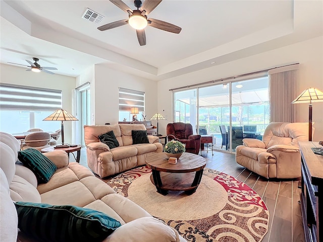 living room with ceiling fan, a tray ceiling, and light wood-type flooring