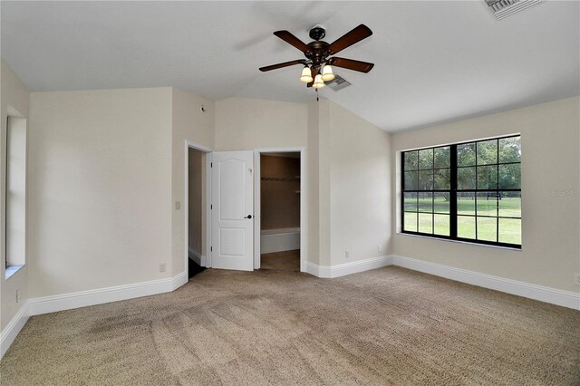 unfurnished bedroom with ceiling fan, light colored carpet, a walk in closet, vaulted ceiling, and a closet