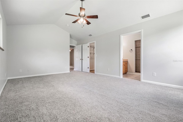 unfurnished bedroom featuring vaulted ceiling, connected bathroom, a spacious closet, light colored carpet, and ceiling fan