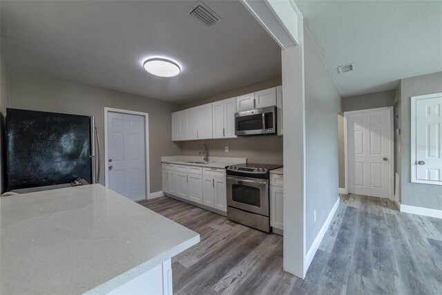 kitchen with stainless steel appliances, sink, white cabinets, and light hardwood / wood-style flooring