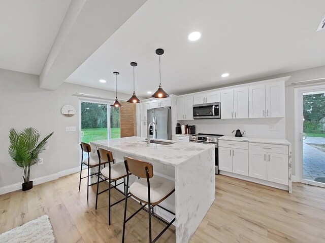 kitchen featuring pendant lighting, white cabinets, a center island with sink, light wood-type flooring, and appliances with stainless steel finishes