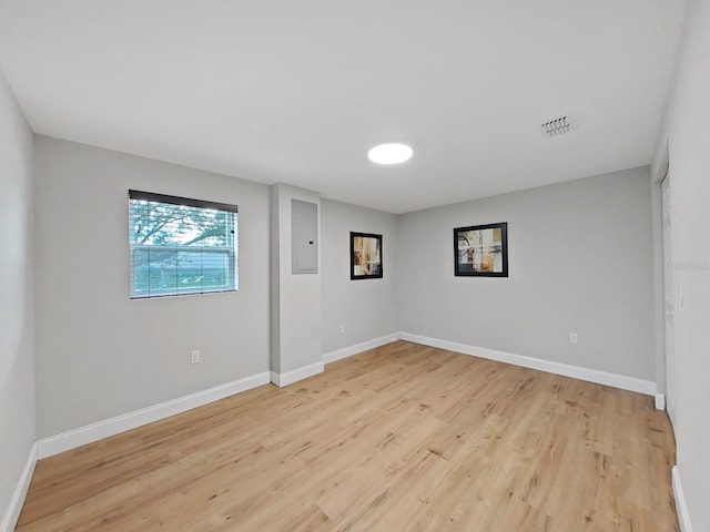 spare room featuring electric panel and light hardwood / wood-style floors